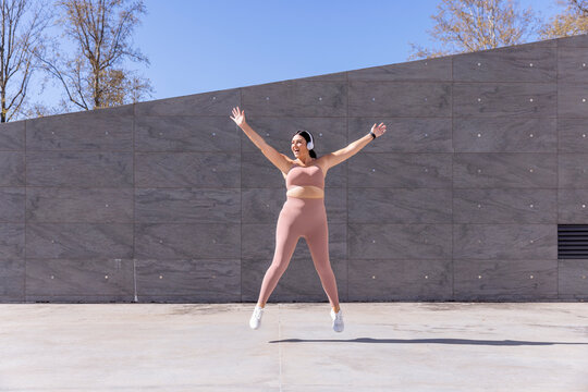 Plus size woman listening music through wireless headphones exercising on footpath