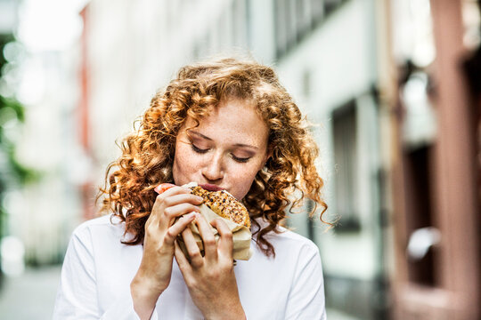 Portrait of young woman eating bagel outdoors