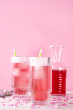 Rose petals iced tea, tasty infused water or lemonade with organic rose syrup, in two tall glasses, with ice cube and rose petals on white pink background