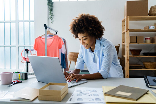 Young female fashion designer using laptop while leaning on desk at studio