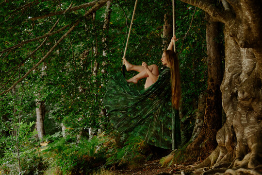 Dreamy fairytale scene swinging barefoot on a forest trapeze