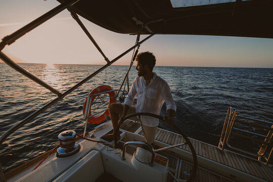 Skipper steering a sailboat on the sea at sunset