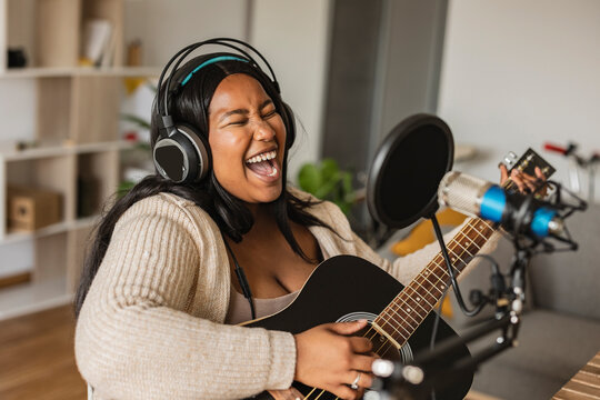 Woman singing and playing guitar on microphone at home