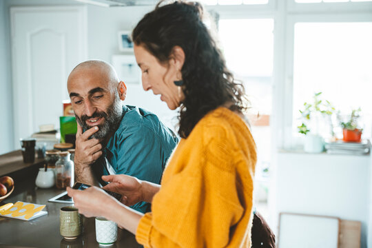 Woman using smart phone by man with hand on chin at home