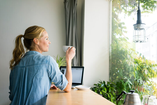 Blond woman sitting in coffee shop, using laptop, drinking coffee