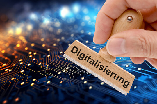 Ein Holzstempel in der Hand ist beschriftet mit dem Aufdruck: Digitalisierung vor einem Hintergrund von digitalen Datenleitungen - FOTOMONTAGE