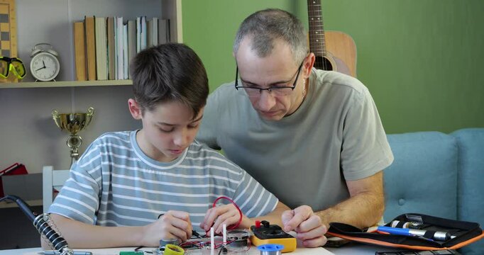 Boy tests electronic circuit with multimeter while father watches attentively and nods with approval. Kid develops practical skills through STEM learning, technology and hands-on education
