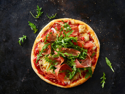 Pizza with ham and rocket on dark ground
