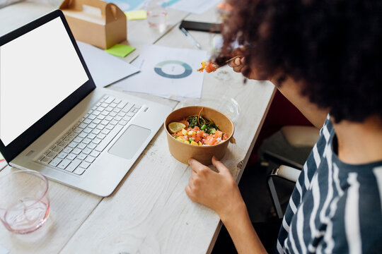 Businesswoman having poke bowl by laptop in lunch break at office