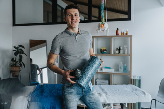 Handsome male physical therapist holding foam roller in practice