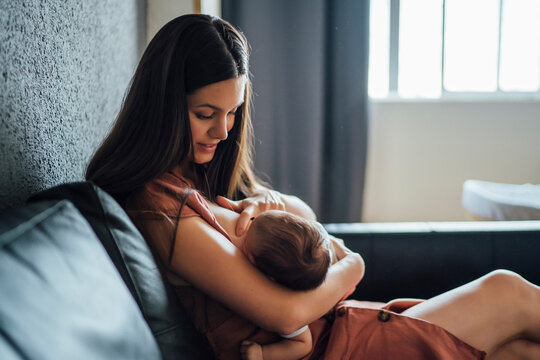 Mother breastfeeding baby boy while sitting on sofa at home