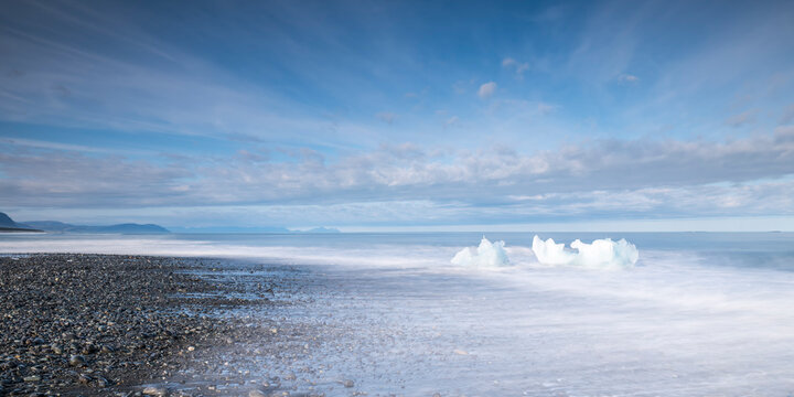 Glacial ice on Diamond Beach with blurred waves in Iceland