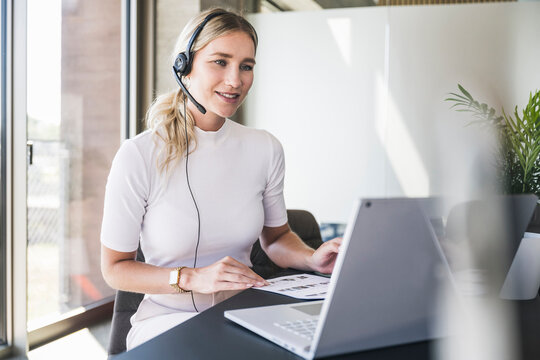 Young customer service representative wearing headset doing video call on laptop at office
