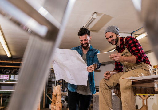 Happy craftsmen examining blueprint through tablet PC at workshop