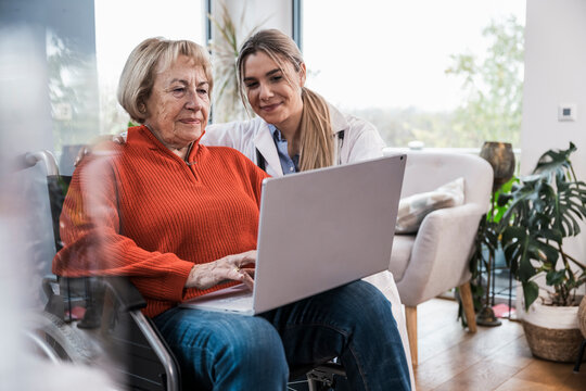 Nurse helping senior patient in wheelchair with a notebook
