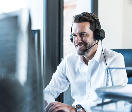Smiling businessman wearing headset working at computer in office