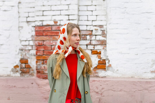 Portrait of a woman in vintage raincoat and red scarf by old brick wall
