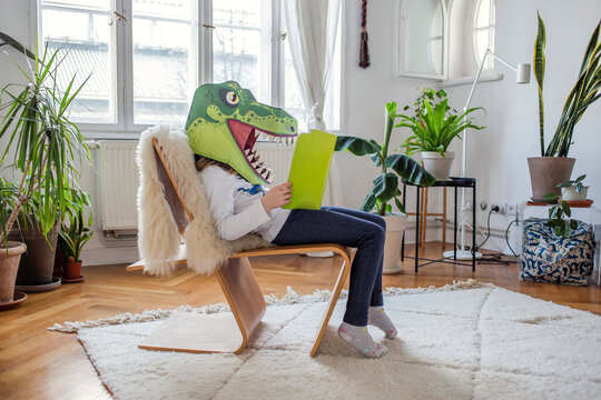 Girl with dinosaur mask reading book at home
