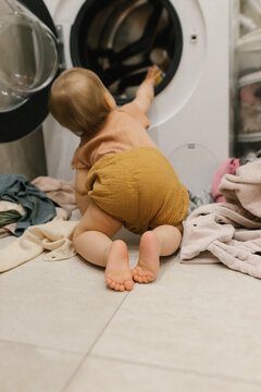 Reaching into an open washing machine surrounded by messy laundry