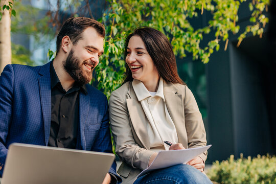 Businessman and businesswoman laughing with laptop outdoors