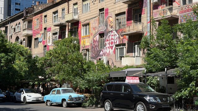 Urban Landscape with Vintage Cars: An intriguing city street scene showcasing a row of eclectic buildings adorned with vibrant graffiti, juxtaposed with vintage cars parked along the sidewalk. Yerevan