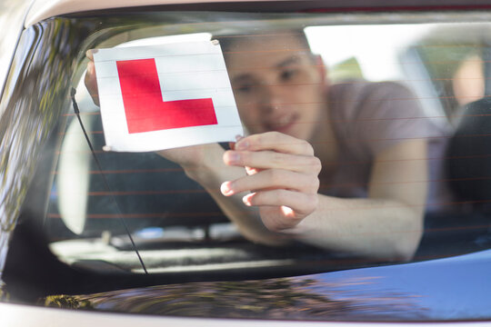 Learner driver placing letter L on rear window of car
