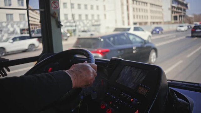 First person view of elderly bus driver hands on steering wheel during city transit drive.