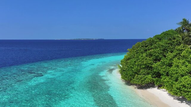 Aerial view of a tropical coastline with a white sand beach, lush green trees, and a vibrant turquoise lagoon in Kendhoo, Baa Atoll, Maldives.