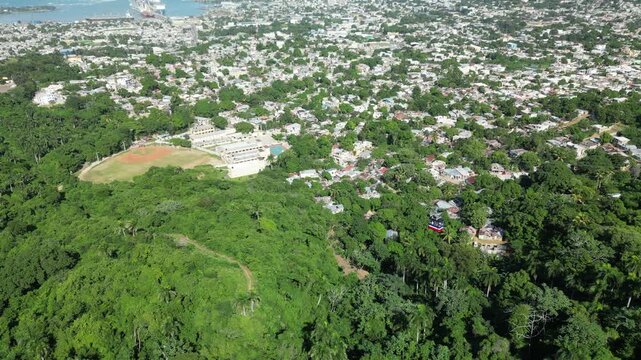 Aerial drone footage featuring the famous Puerto Plata cable car cabin ascending Mount Isabel de Torres above lush tropical forest with panoramic views of Puerto Plata city and the Atlantic coastline 