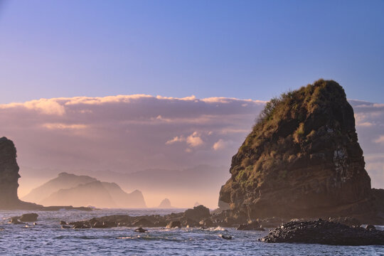 Sunrise over rugged Papuma coast with dramatic rocks and golden light reflecting on waves. Jember, Indonesia. 