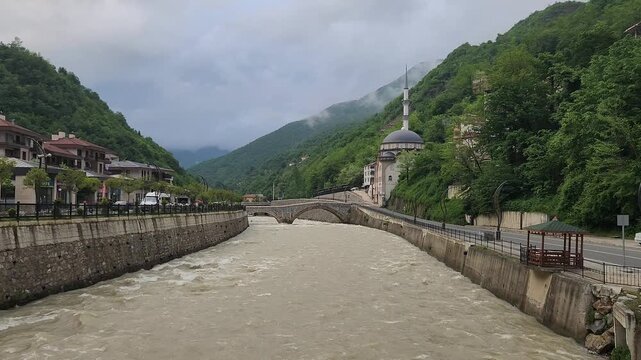 Aksu Stream in Dereli, Giresun, flowing from the Karag&ouml;l Mountains toward the Black Sea, with a historic bridge spanning its fast-flowing waters amid a rural landscape.