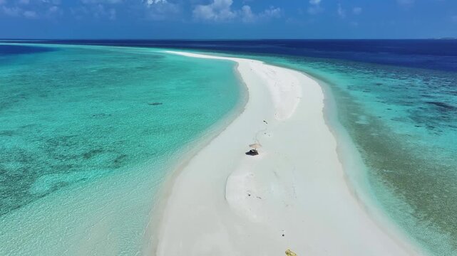 Aerial view of a long white sandbank stretching into the turquoise and deep blue ocean under a clear sky in Kendhoo, Baa Atoll, Maldives.