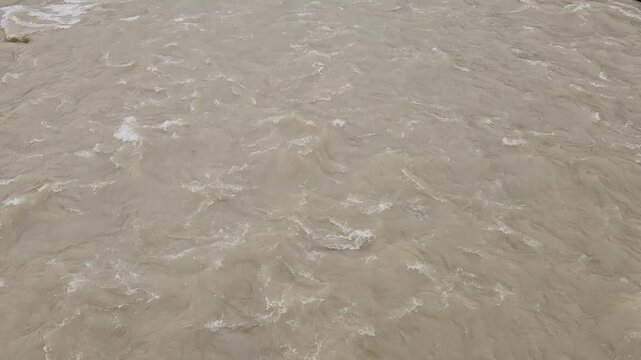 A swollen stream surges with muddy brown water after heavy spring rains, showcasing the force of seasonal flooding and rapid runoff in a natural landscape.