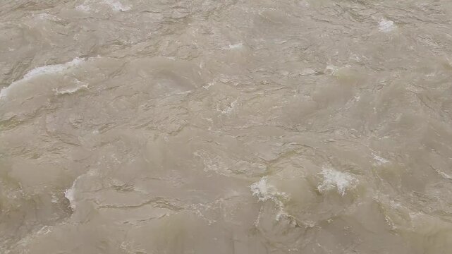 A swollen stream surges with muddy brown water after heavy spring rains, showcasing the force of seasonal flooding and rapid runoff in a natural landscape.