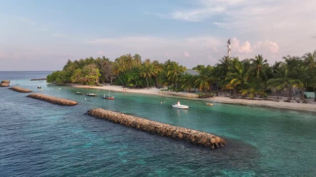 Aerial view of the tropical island of Kendhoo with lush palm trees, white sand beaches, and stone breakwaters in the turquoise ocean, Kendhoo, Baa Atoll, Maldives.