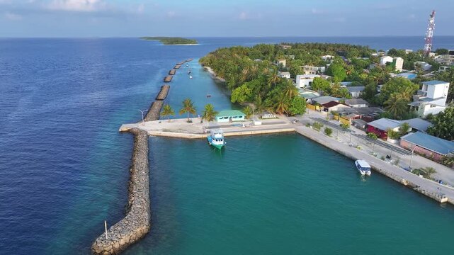 Aerial view of the harbor and stone breakwater with boats moored in turquoise waters along the lush tropical coastline of Kendhoo, Baa Atoll, Maldives.