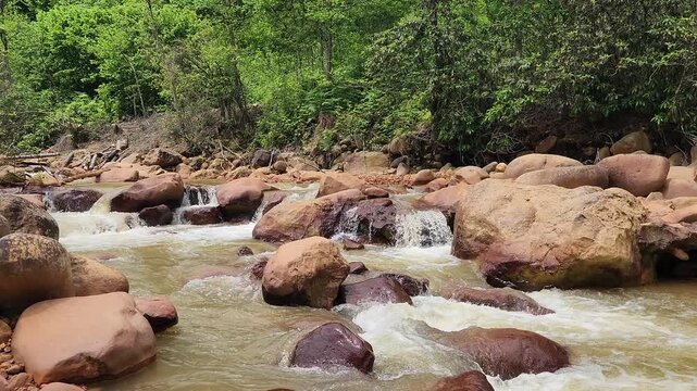 A stream colored red-orange by mining pollution, showing acid mine drainage effects where dissolved metals oxidize and form iron-rich sediments in the water and riverbed.