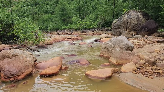 A stream colored red-orange by mining pollution, showing acid mine drainage effects where dissolved metals oxidize and form iron-rich sediments in the water and riverbed.