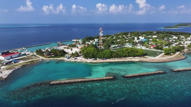 Aerial view of Kendhoo island featuring a communication tower, football pitch, and lush tropical vegetation surrounded by turquoise water in Kendhoo, Baa Atoll, Maldives.