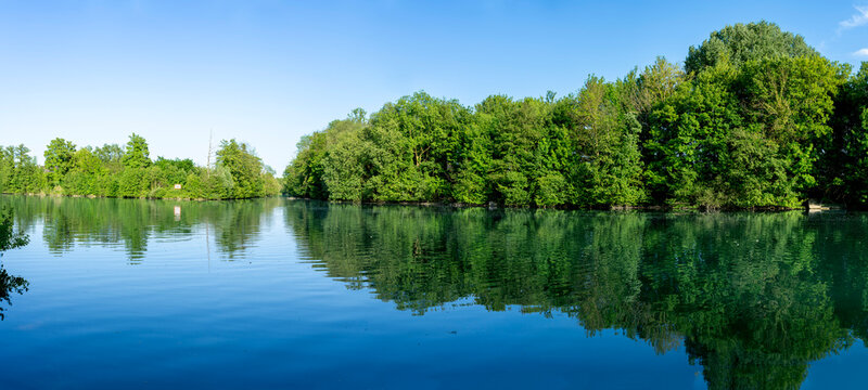 Chateau-Thierry, France - 05 01 2026: Panoramic view of the Marne river and trees reflecting on the water along the towpath with sunny blue sky