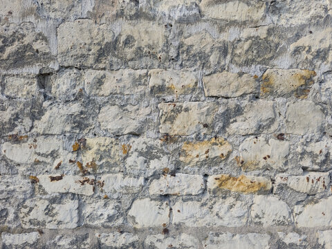 Rough weathered old stone wall texture background with irregular grey, white, and yellow stones and visible mortar.