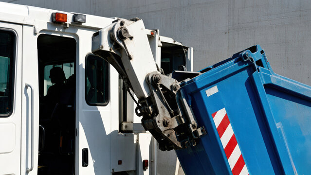 Garbage truck lifting a blue dumpster for waste collection. Mechanical arm emptying trash bin for municipal sanitation services