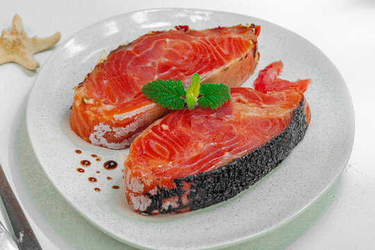 Raw salmon steaks on a ceramic plate garnished with mint, with cutlery on a white background