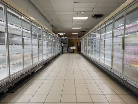 Empty refrigerator and freezer cabinets in a deserted supermarket aisle, illustrating concepts of food shortage, supply chain issues, or panic buying.