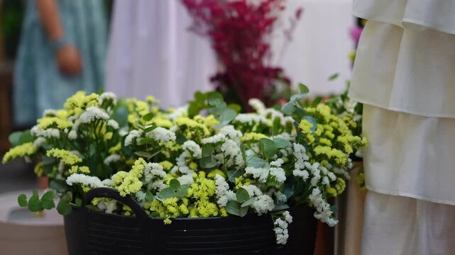 Beautiful bouquet of yellow, white, and green statice flowers in a black basket. An event decoration with people moving in the background