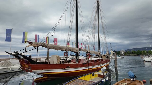 Bardolino, Italy - May 14, 2026 - Historic wooden sailing ship docked in a harbor with flags and Ferris wheel in background