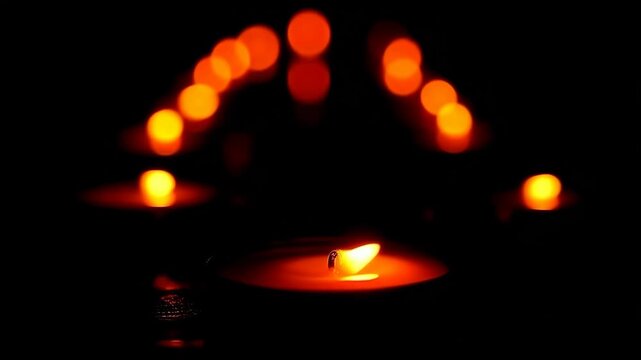 Cinematic slow motion of multiple burning tealight candles arranged in a row slowly fading out. Abstract concept of memory loss, dying hope, memorial day tribute, or end of a life cycle.