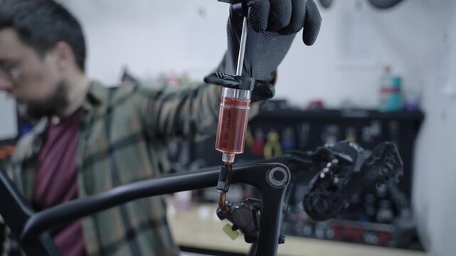 Professional male mechanic bleeding hydraulic brakes on expensive black carbon road bike. Technical maintenance of premium racing bicycle, fluid service with syringe tool in modern workshop.