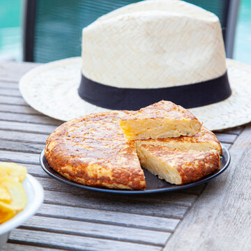Spanish potato omelet on a wooden table with a summer hat.