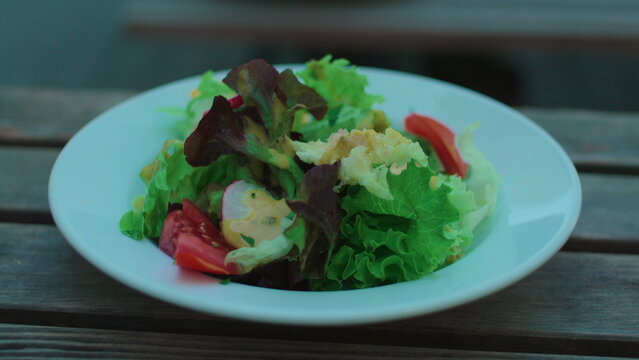 Fresh garden salad served on wooden outdoor dining table capturing healthy eating, vegetarian cuisine and authentic casual restaurant lifestyle